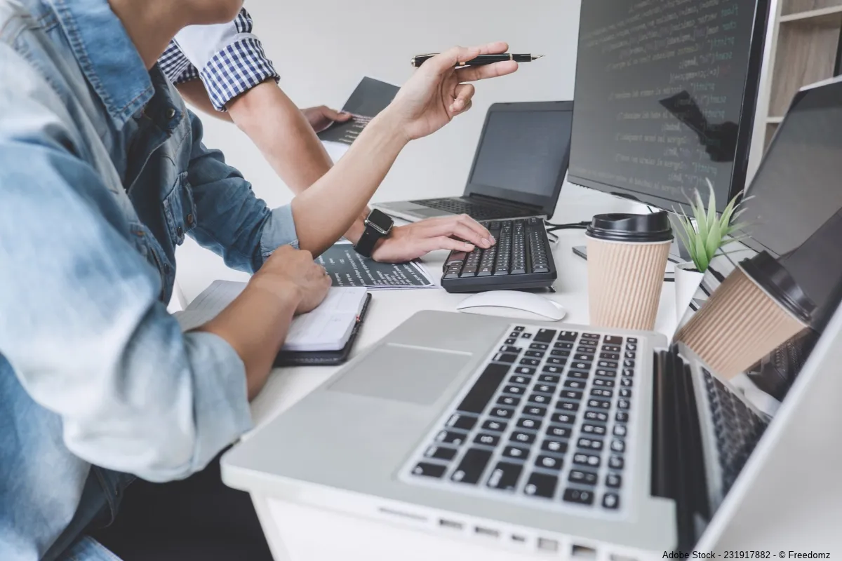 Zwei Personen arbeiten gemeinsam an mehreren Computern und besprechen Programmierung sowie Software Kosten Steuererklärung im modernen Büro.
